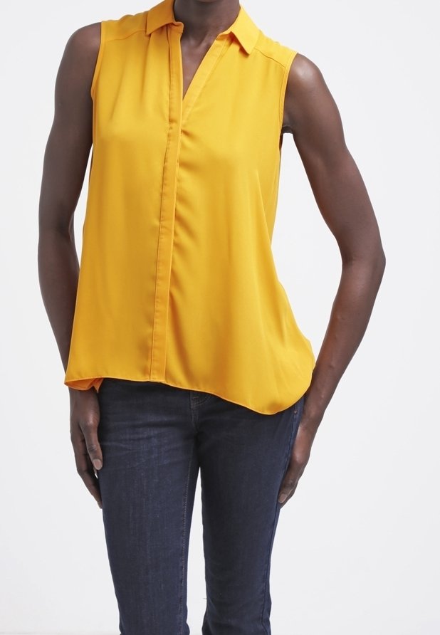 Žlutá bez rukávů halenka s límečkem, se zapínáním na přední části a asymetrickým lemováním. Nosit s tmavými džíny. Hladká textilie.