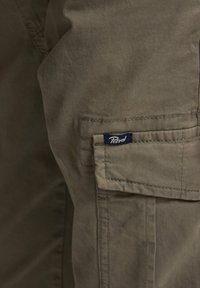 Katoenen cargobroek in olijfgroen met een zijzak en een marineblauw label. Heeft stevige stiksels en een licht gestructureerde afwerking.