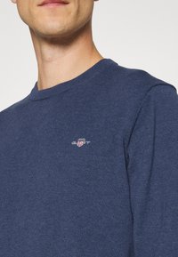 Navyblauer Rundhals-Pullover aus Strickstoff mit einem kleinen gestickten Logo auf der Brust. Glatte Textur und figurbetontes Design.