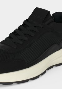Baskets noires à lacets avec panneaux latéraux côtelés, zone des orteils texturée, languette siglée et semelle blanche épaisse avec semelle noire.