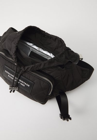 Black quilted backpack with a drawstring closure, silver interior, front zip pocket, and logo patch. Adjustable strap and smooth hardware.