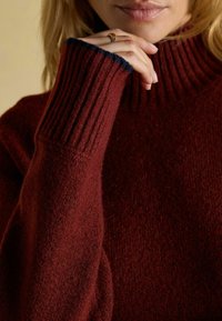 Burgunderfarbener Wollpullover mit einem hohen Rippenkragen, gerippten Bündchen mit marineblauen Akzenten und einer strukturierten Oberfläche am Körper.