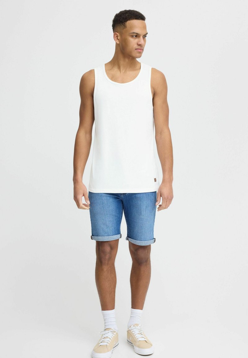 Top blanco sin mangas, shorts de mezclilla azul con dobladillo, calcetines blancos y zapatillas beige. Tejido suave, diseño casual, forma ajustada.