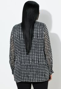 Sort og hvid gennemsigtig bluse med prikmønster over hele, lange ærmer og en løs pasform. Glat stof med en let følelse.