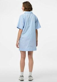 Robe chemise en coton bleu clair avec des manches courtes, un col et une coupe droite, comportant un détail de couture au dos et un style minimaliste.