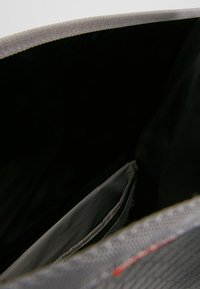 Interno grigio di una borsa con fodera nera, caratterizzato da una piccola tasca grigia. Il materiale appare liscio con un bordo texturizzato.