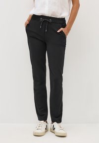 Sorte joggerbukser lavet af blødt stof, med elastisk talje med snor, sidelommer og tapered ben. Kombineret med hvide sneakers.