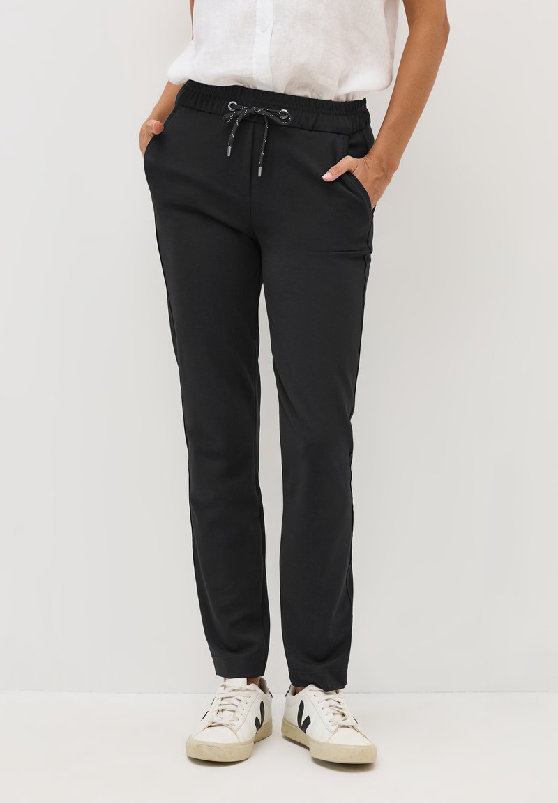 Sorte joggerbukser lavet af blødt stof, med elastisk talje med snor, sidelommer og tapered ben. Kombineret med hvide sneakers.