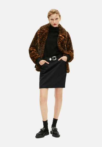 Bruine nepbontjas met dierenprint, zwarte coltrui, zwarte kokerrok en glanzende zwarte schoenen met gespaccenten.
