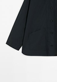 Mörk marinblå knappad jacka med långa ärmar och en stor fyrkantig framficka på vit bakgrund.