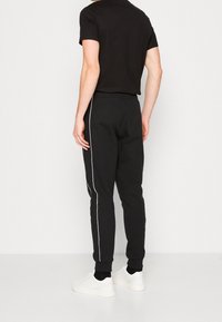 Black jogger pants with white side stripes, elastic waistband, and cuffed hems, paired with a fitted black t-shirt and white sneakers.