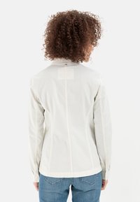 Jasnoszara, dopasowana kurtka z podniesionym kołnierzem, detalami szwów i gładką teksturą, widziana z tyłu na jednolitym tle.