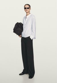 Witte oversized blouse met knopen, zwarte wijde broek, zwarte zonnebril en een zwarte tas. Gelijke texturen, casual ontwerp.