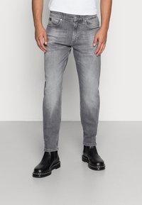 Jeans de mezclilla gris con corte recto, que presentan un diseño clásico de cinco bolsillos y un ligero desgaste, combinados con botas de cuero negro hasta el tobillo.