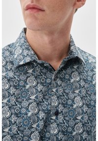 Musterhemd mit Knöpfen, das ein blau-weißes Blumenmuster, einen klassischen Kragen und eine subtile Textur aufweist. Zwei Knöpfe sind am Hals sichtbar.