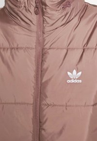 Giacca puffa marrone in materiale lucido con colletto alto, dotata di zip frontale e logo Adidas bianco sul lato sinistro del petto.