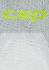 Tessuto grigio lavorato a maglia con la parola neon gialla "cep" sopra un motivo triangolare grigio chiaro e bianco.