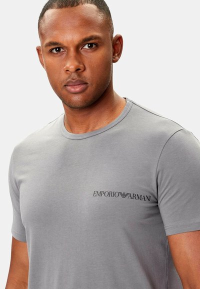 Harmaa puuvillainen t-paita, jossa on pyöreä pääntie ja lyhyet hihat. Vasemmassa rintataskussa on musta "Emporio Armani" -logo. Sileä pinta.