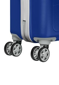 Blauwe hard-shell koffer met een gestructureerd oppervlak, zilveren rits en vier multidirectionele zwarte wielen met een grijs hub ontwerp.