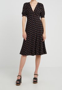 Vestido negro con escote en V y mangas abullonadas, adornado con un pequeño patrón floral rojo. Diseño acampanado en A, textura suave, hasta la rodilla.