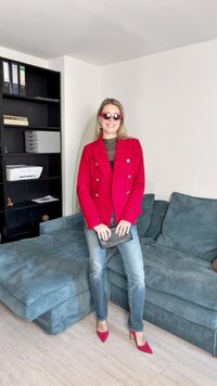 Piros, dupla gombos blézer arany gombokkal, fekete áttetsző felső, világoskék farmernadrág és piros hegyes sarkú cipő. Kicsi fekete clutch táska.