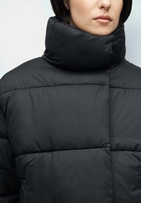 Čierna prešívaná bunda s vysokým golierom, s prešívanými časťami a hladkou textúrou. Bez viditeľných zapínaní alebo ozdôb.