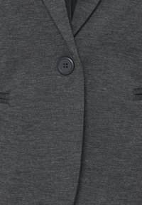 Veste en tissu gris foncé avec un grand bouton noir fixé à l'avant et deux poches horizontales fentes de chaque côté.