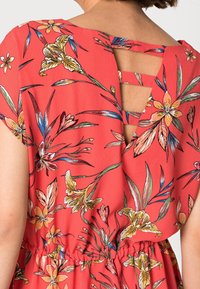 Rød blomsterkjole med udskåret ryg, korte ærmer, elastisk talje og detaljerede illustrationer af blomster i gult, grønt og blåt.