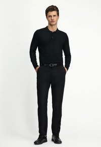 Schwarzes Poloshirt mit langen Ärmeln und Kragen, kombiniert mit schwarzen Hosen und schwarzen Schuhen. Glatte Textur, figurnahe Passform und minimalistischer Stil.