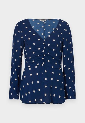 Marineblouse met lange mouwen, voorzien van witte stippen, een V-hals en een geplooid detail aan de voorkant. Glad stof met een vloeiend ontwerp.