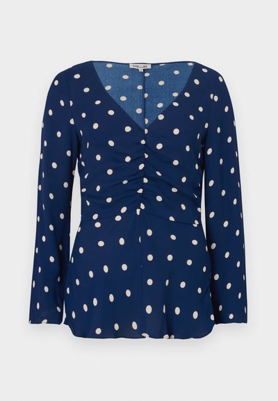 Μπλε μπλούζα με μακριά μανίκια, διακοσμημένη με λευκές πουά, λαιμόκοψη σε σχήμα V και συγκέντρωση στο μπροστινό μέρος. Λείο ύφασμα με ρέουσα σχεδίαση.