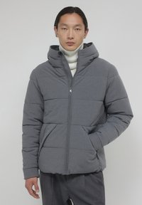 Giacca a vento grigia con cappuccio, dotata di chiusura con zip, polsini a coste e due tasche laterali. Texture opaca con design trapuntato.