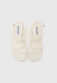 Hvide slingback sandaler med firkantet tå, glat syntetisk overdel og tynde krydsede stropper. Inkluderer justerbar ankelrem med metalspænde.