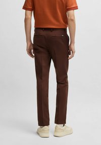 Bruna byxor i slät tyg, slim fit, med två bakfickor. Bärs med en orange topp och ljusa sneakers.