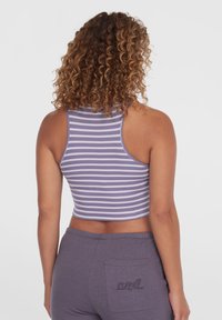 Fialový a bílý pruhovaný crop top s vysokým výstřihem a ribbovanou texturou, kombinovaný s fialovými tepláky s logem na zadní kapse.