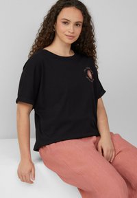 Zwarte katoenen t-shirt met korte mouwen en een ruime pasvorm. Heeft een roze graphic met de tekst "Vul je dagen met zonneschijn" nabij de borst.