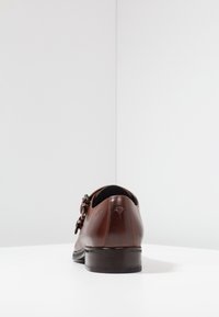 Chaussure en cuir marron avec un bout arrondi, accent de boucle et petit talon empilé. Texture lisse avec un détail de marque subtil à l'arrière.