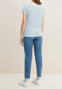 Pruhovaná modro-bílá košile s krátkým rukávem v kombinaci se světle modrými džínami, které mají volný střih a ohrnuté lemování, doplněná bílými teniskami.