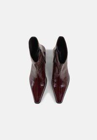 Bottines brillantes rouge foncé avec bouts pointus et fermetures éclair latérales, vues de dessus sur un fond clair.