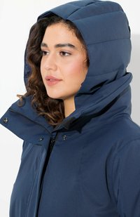 Giacca puffer blu navy con colletto alto e cappuccio oversize. Presenta una cerniera frontale e chiusure a bottoni automatici per una vestibilità sicura.