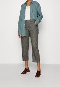 Gestreepte teal overhemden, een witte tanktop eronder, grijze op maat gemaakte cropped broek en bruine leren loafers met blokhak.