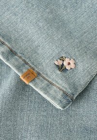 Denim tkanina u svijetloplavoj boji, s izveznim cvjetnim uzorkom u ružičastoj i zelenoj boji. Na rubu se nalazi smeđa kožna oznaka.