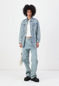 Lys blå denimjakke med to frontlommer, paret med matchende denimbukser med distinkte sømdetaljer, og svarte platåsko.