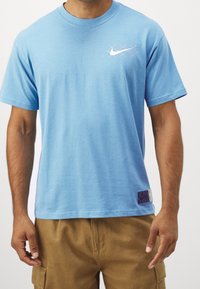 Tyrkysové bavlněné tričko s kulatým výstřihem, krátkými rukávy a malým bílým logem Nike. Obsahuje texturovanou fialovou jmenovku na lemu.