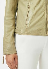 Giacca in pelle verde chiaro con tasca con zip e dettagli di cucitura sottili. Maniche lunghe con chiusura a zip sui polsini.