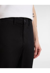 Pantaloni in denim nero con una texture liscia, dotati di chiusura con zip e bottone. Hanno tasche laterali e un design aderente.