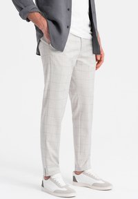 Pantaloni a quadri grigio chiaro con vestibilità slim, realizzati in materiale tessuto. Presentano spacchi laterali all'orlo e sono abbinati a sneakers bianche.