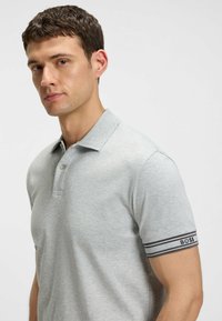 Polo shirt grigio chiaro realizzato in tessuto morbido, con colletto a bottoni e accenti a strisce nere e grigie sulle maniche.