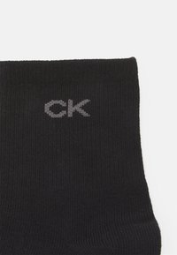 Čierne rebrované ponožky vyrobené z mäkkého materiálu s šedým logom "CK" pleteným pri manžete. Jednoduchý dizajn bez ďalších vzorov alebo akcentov.