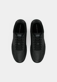 Paire de baskets noires Tommy Hilfiger avec lacets, logos sur les languettes et les côtés, vues de dessus sur un fond blanc.